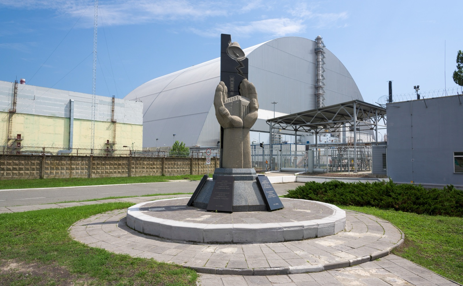 El Nuevo Confinamiento Seguro, el gran arco de acero que cubre el reactor 4 de Chernóbil, detrás de un monumento a quienes trabajaron tras el accidente, en julio de 2018.
